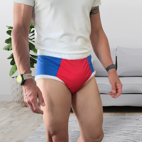 A man wearing red, blue, and white color-blocked adult cloth diaper, paired with a white t-shirt, standing in a living room setting.