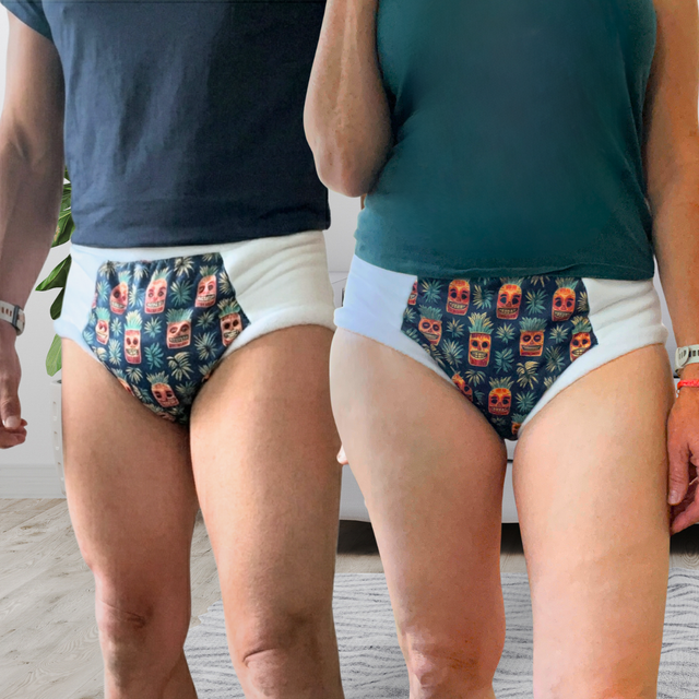 Two models shown from the waist down wearing adult cloth diapers with a colorful tropical skull and palm leaf patterned pouch on the back side.